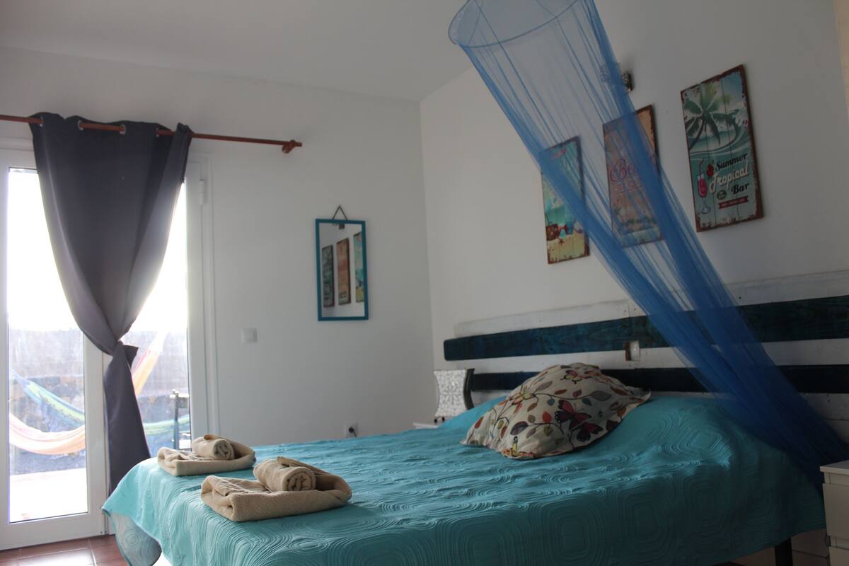 Quarto com cama, janela com cortinas e decorações nas paredes.