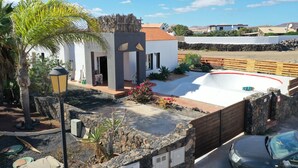 A modern house with a swimming pool, surrounded by a stone wall and a wooden fence. - Da Mata Kite&Surf House (La Oliva)