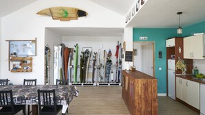A spacious kitchen with wooden cabinets, a wooden dining table with chairs, and a surfboard hanging from the ceiling. - Da Mata Kite&Surf House (La Oliva)