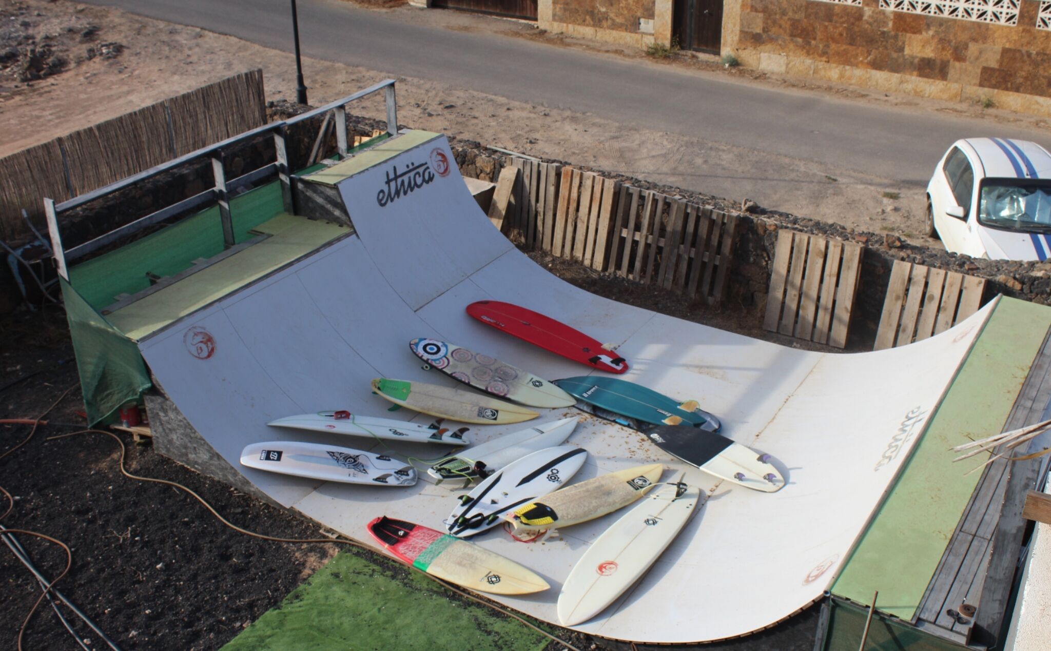 A skate ramp with various surfboards and a car parked nearby.