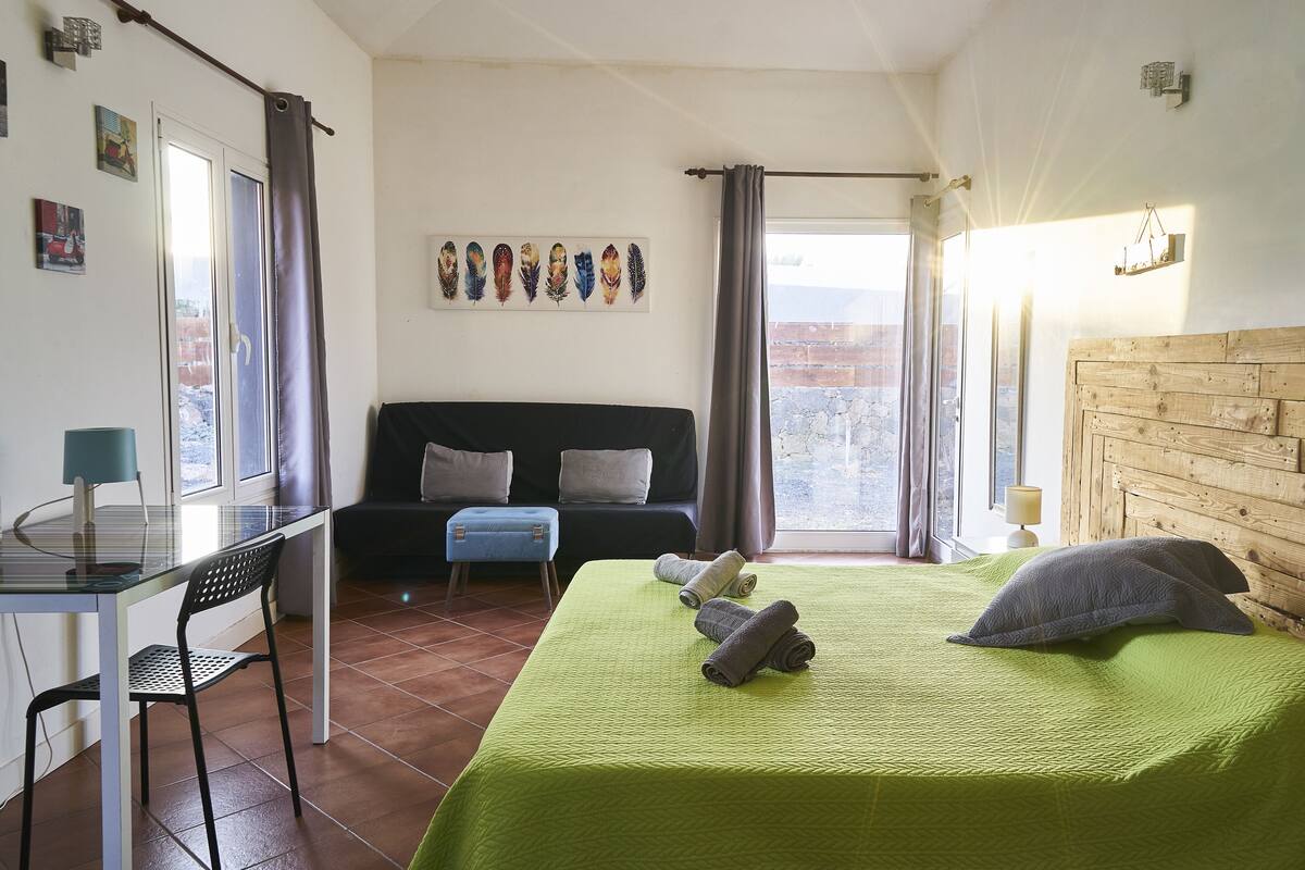 Quarto com cama, escrivaninha, cadeira, sofá e janela com cortinas.
