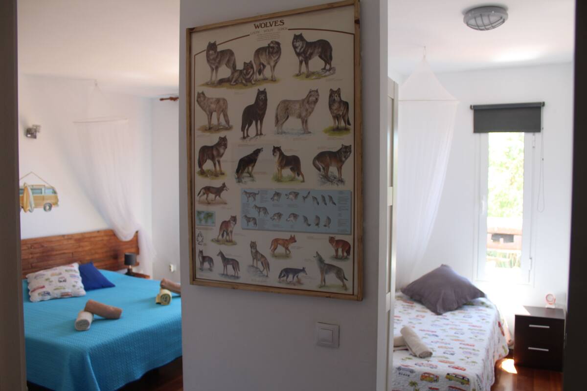 Quarto com duas camas, um cartaz de lobos na parede e janela com vista para vegetação.