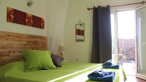 A bedroom with a wooden headboard, a green bedspread, and a view of a garden through a sliding door. - Da Mata Kite&Surf House (La Oliva)