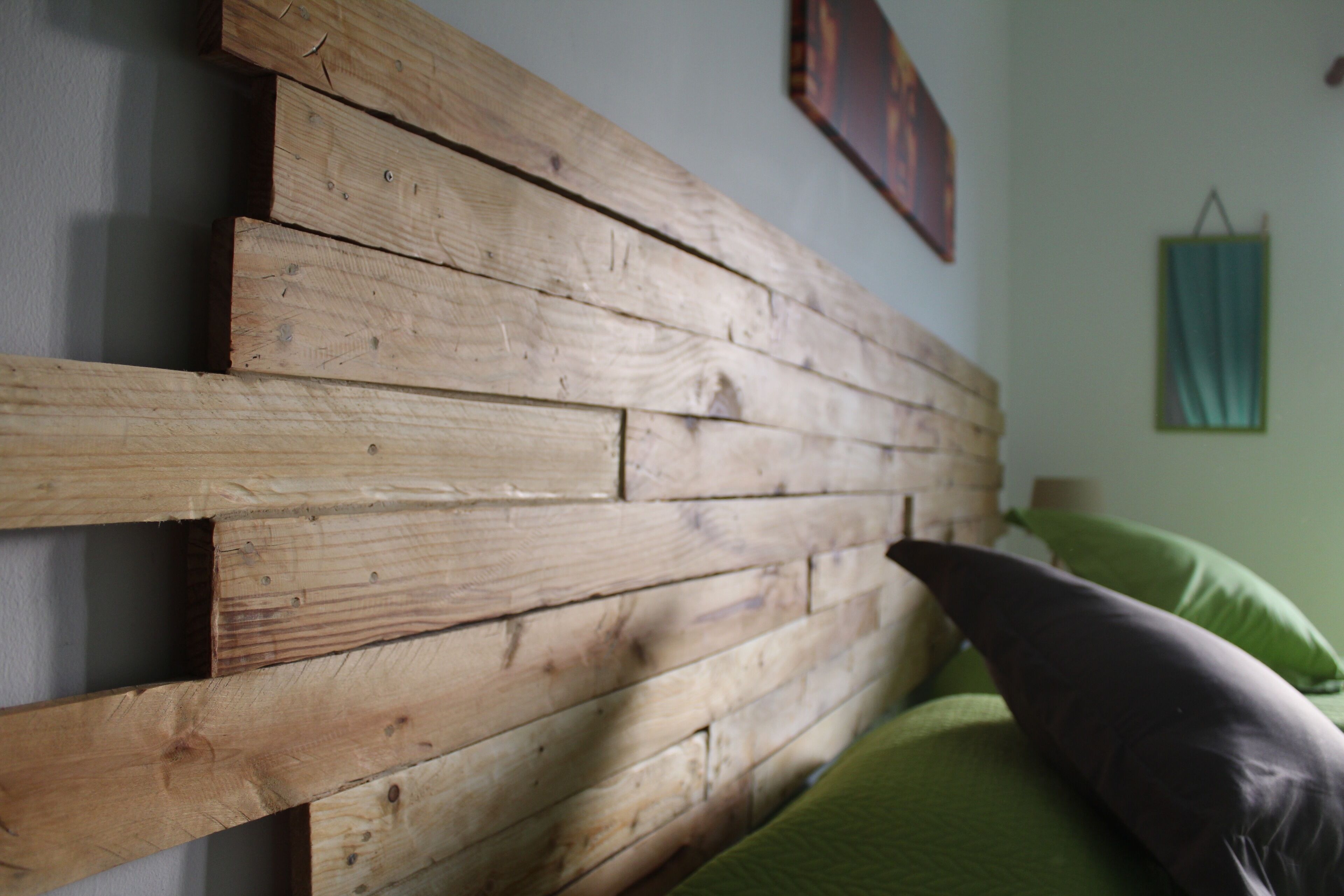 A wooden headboard against a wall with a green pillow and a framed picture above it.