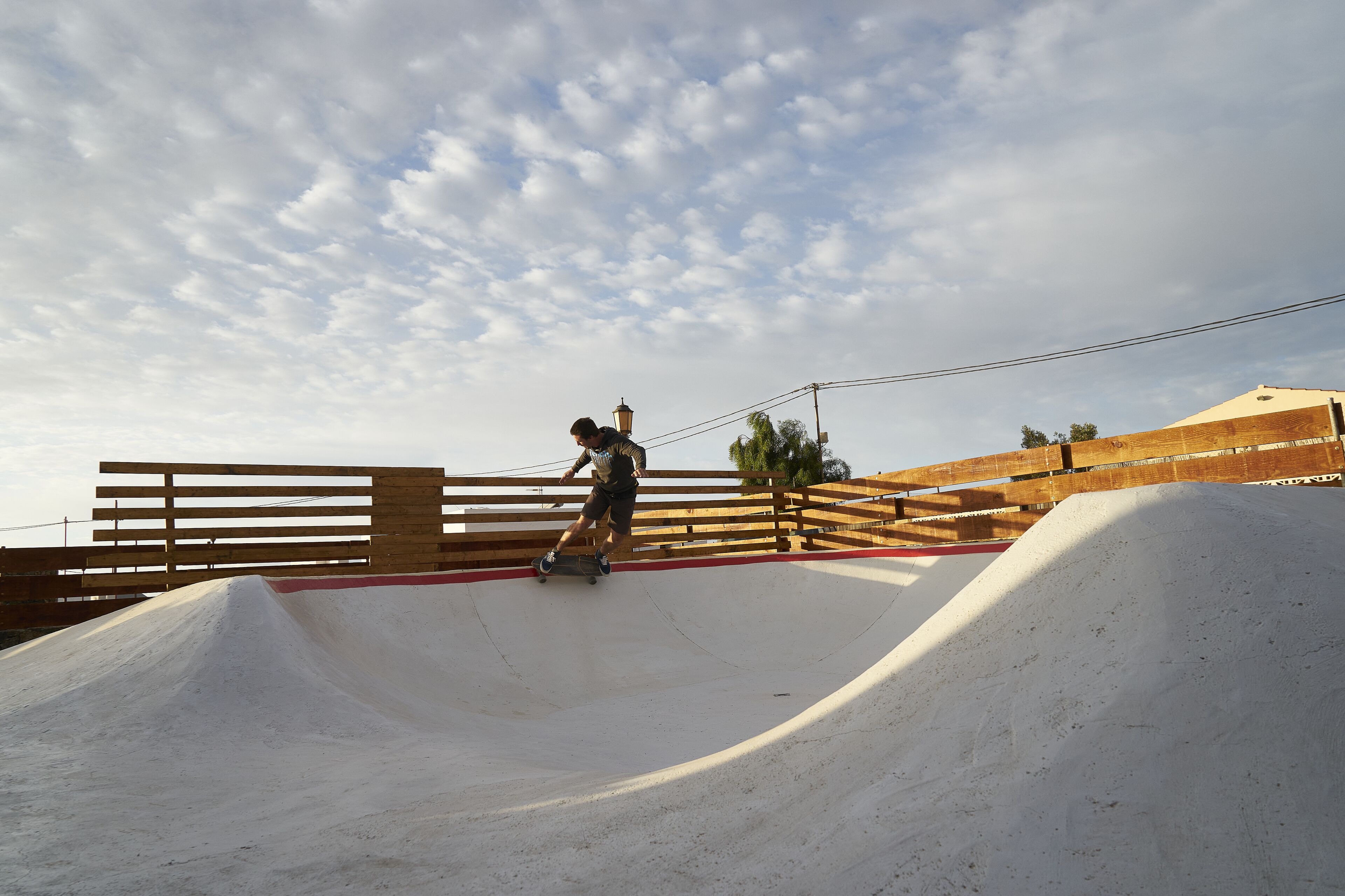 Un patinador en un parque de skate con rampas de madera y cielo despejado.