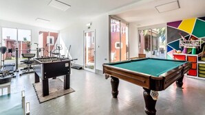 Une table de billard, du matériel d’exercice et un mur aux motifs géométriques et aux couleurs vives, le tout dans un espace intérieur bien éclairé.