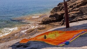 A beach scene with a purple umbrella and a colorful towel on rocks. - Seafront Aegeans blue pearl over infinity pool (Keratea)