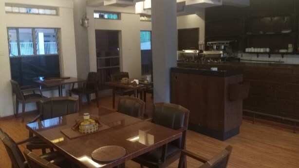 A spacious dining area with a wooden table and chairs, a kitchen area with a bar, and a view of the outside through large windows. - Haridge Inn (Nairobi)