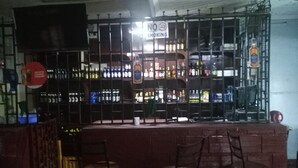 A bar area with a 'No Smoking' sign, shelves of liquor bottles, and two wooden chairs. - Haridge Inn (Nairobi)