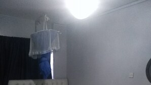 A bedroom with a bed, a bedside table, a hanging light fixture, and a window with curtains. - Haridge Inn (Nairobi)