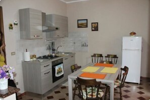 Une cuisine équipée d’une cuisinière, d’un évier et d’un réfrigérateur. On y trouve une table à manger avec des chaises et un vase de fleurs.
