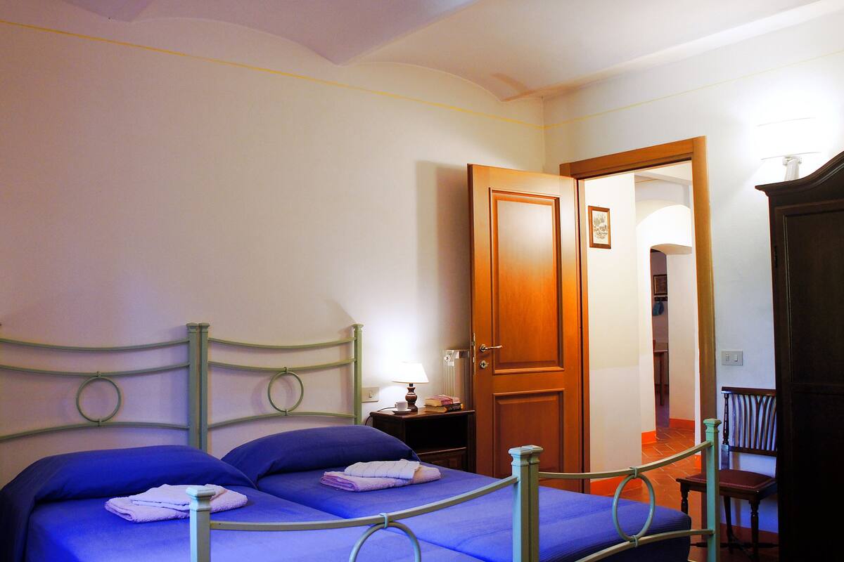 Une chambre à coucher avec un lit, une table de chevet, une lampe, une porte en bois et une chaise.