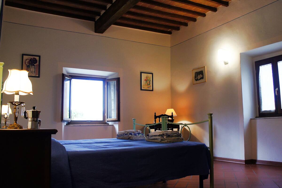 Une chambre à coucher avec un lit, une fenêtre, une chaise et une table avec une lampe.