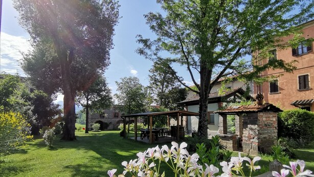 Ein Garten mit einem Pavillon, Steinmauern und einem Gebäude im Hintergrund.
