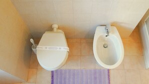 Une salle de bain avec des toilettes et un bidet, tous deux de couleur blanche, et un tapis violet sur le sol.