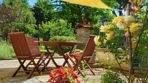 Eine Terrasse im Freien mit einem Holztisch und -stühlen, umgeben von viel Grün und einem gelben Sonnensegel.