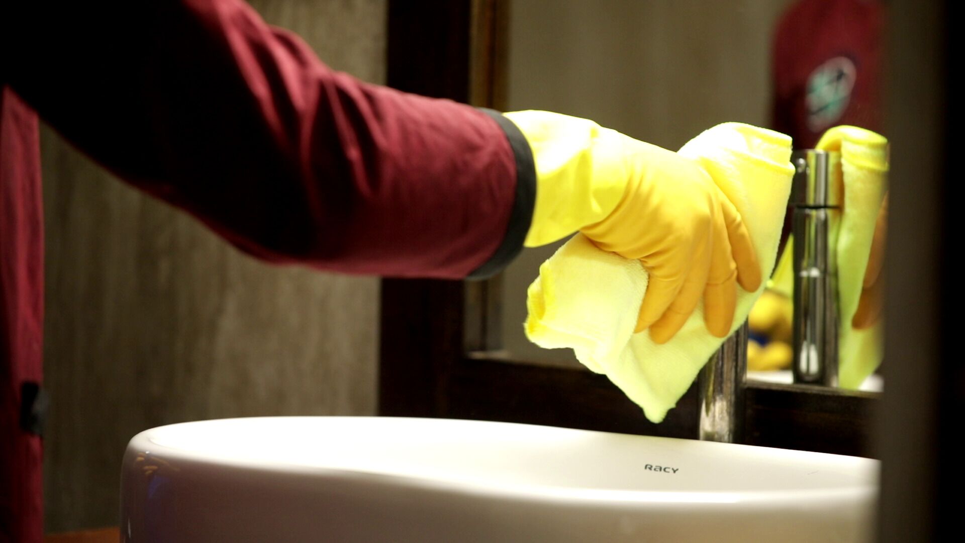 A hand cleaning a sink with a yellow cloth.