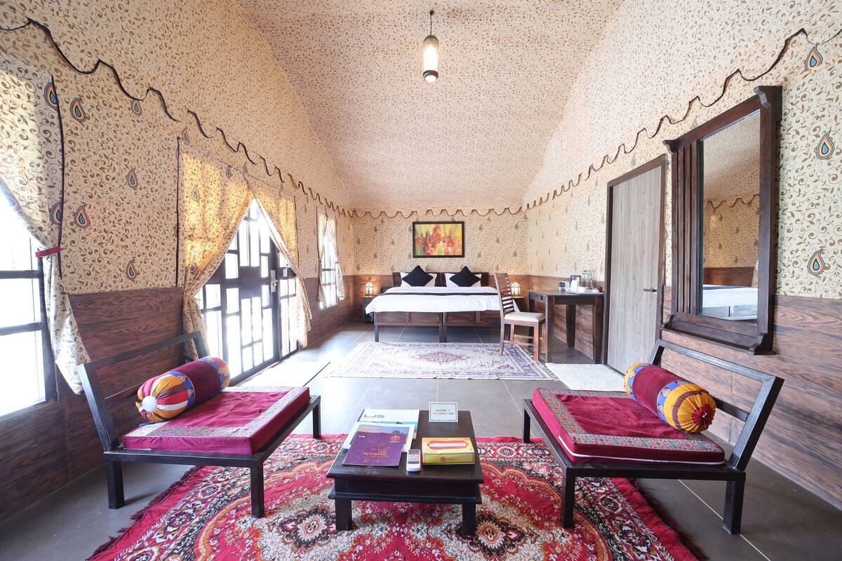 A room with a bed, two chairs, a table, and a mirror.