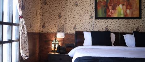 A hotel room with a bed, a nightstand with a lamp, a telephone, and a window with curtains.