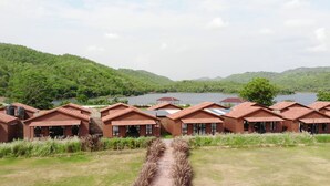 A row of wooden cabins with a view of a lake and forested hills. - Statue Of Unity Tent City (Garudeshwar)
