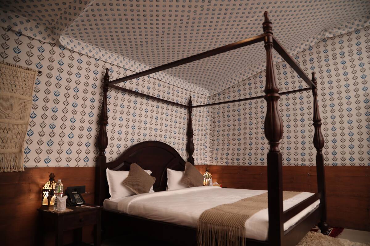 A four-poster bed with a wooden headboard, white bedding, and a patterned wallpaper background.