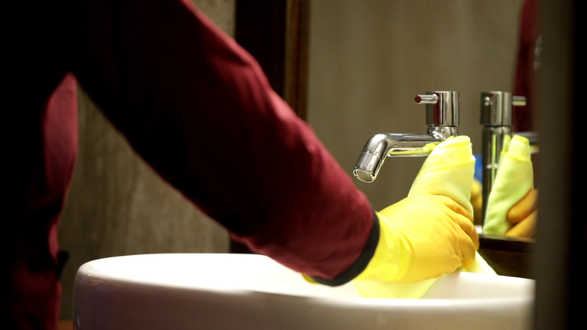 A person wearing yellow gloves and a maroon sleeve operating a faucet.