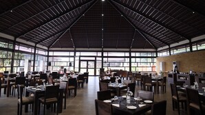 A spacious dining area with high ceilings and large windows, featuring multiple tables and chairs arranged for dining. - Statue Of Unity Tent City (Garudeshwar)
