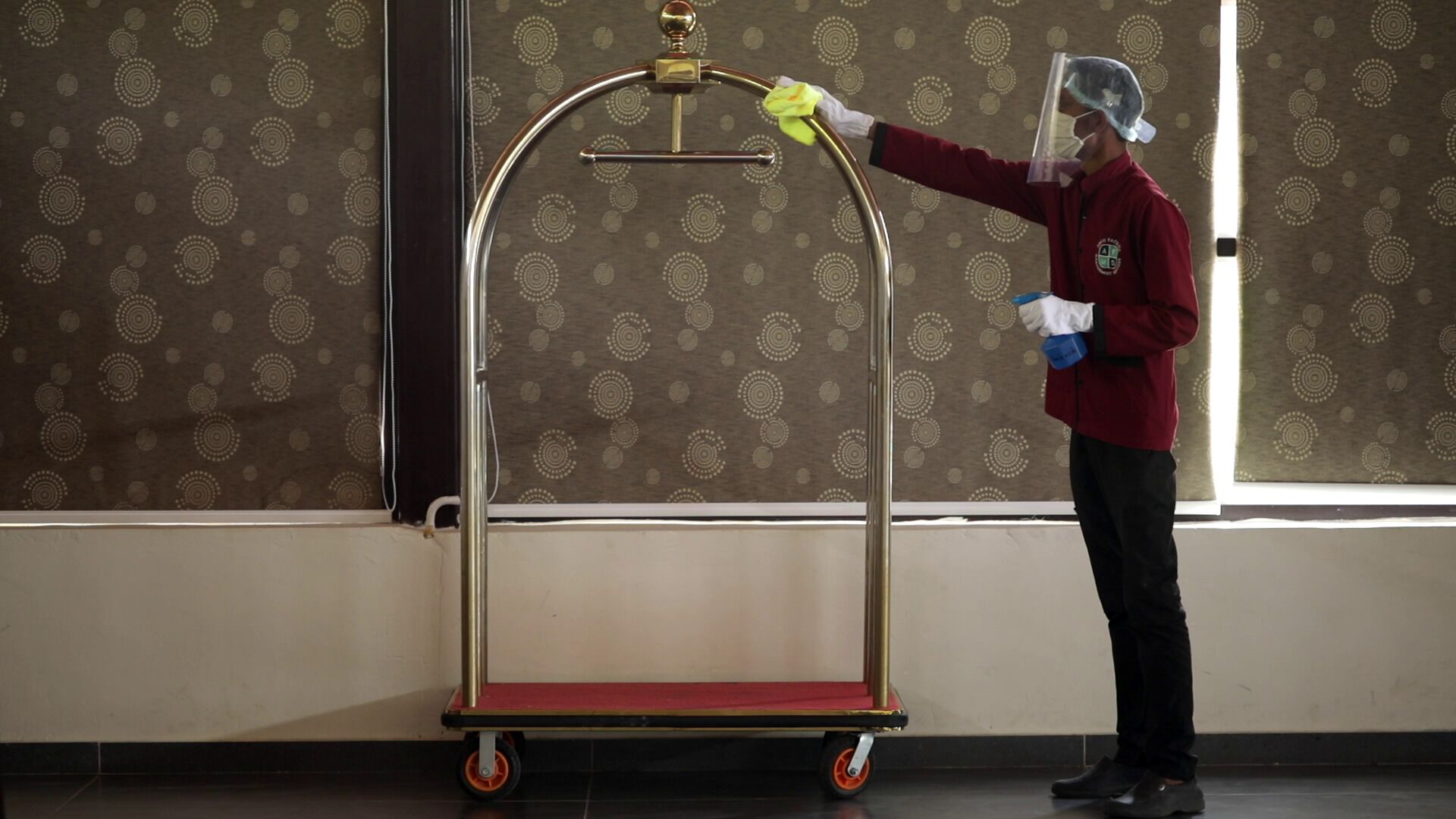 Een persoon in een rood uniform maakt een kamer schoon met een schoonmaakkar.