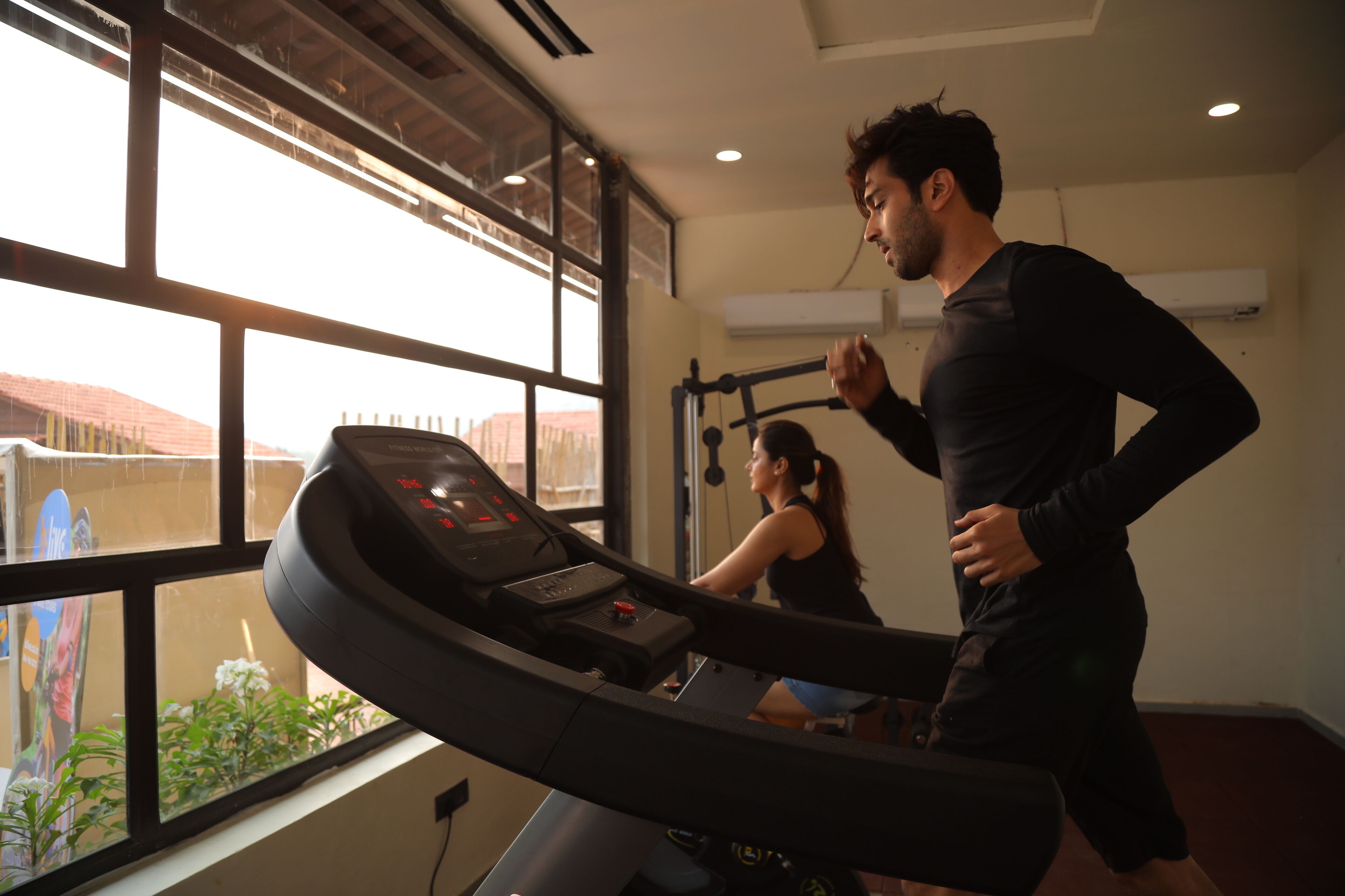 A gym with a treadmill, a woman exercising, and a man running.