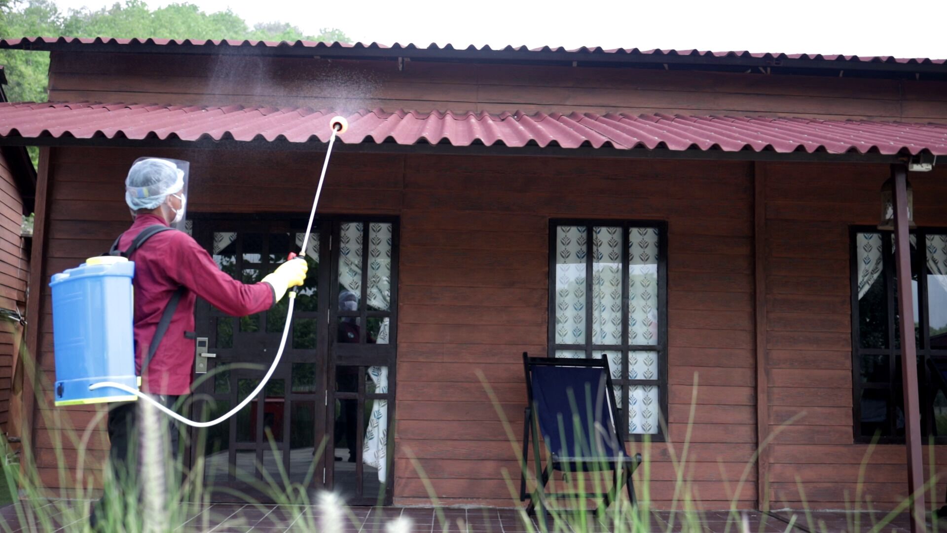 Une personne utilise un nettoyeur haute pression pour nettoyer l’extérieur d’une maison en bois dont le toit est rouge.