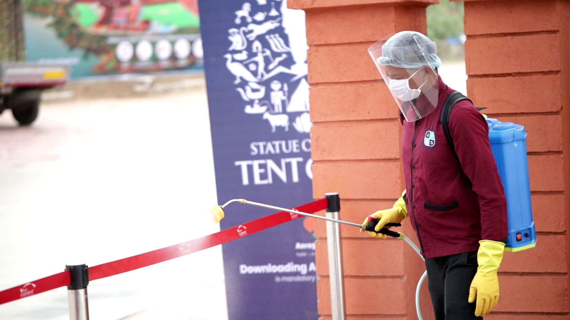 A person wearing a protective suit and mask, using a sprayer near a red barrier.
