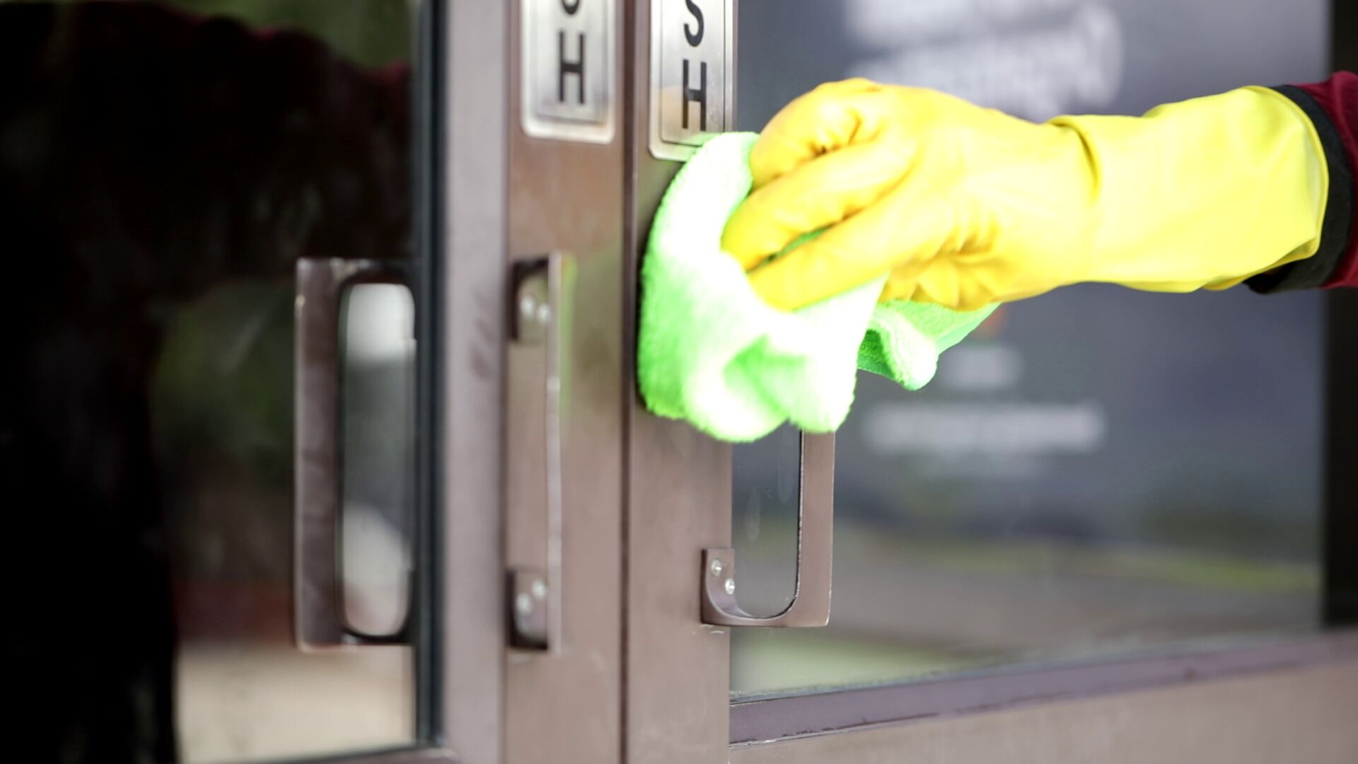 Eine Hand reinigt einen Türgriff aus Glas mit einem Tuch.