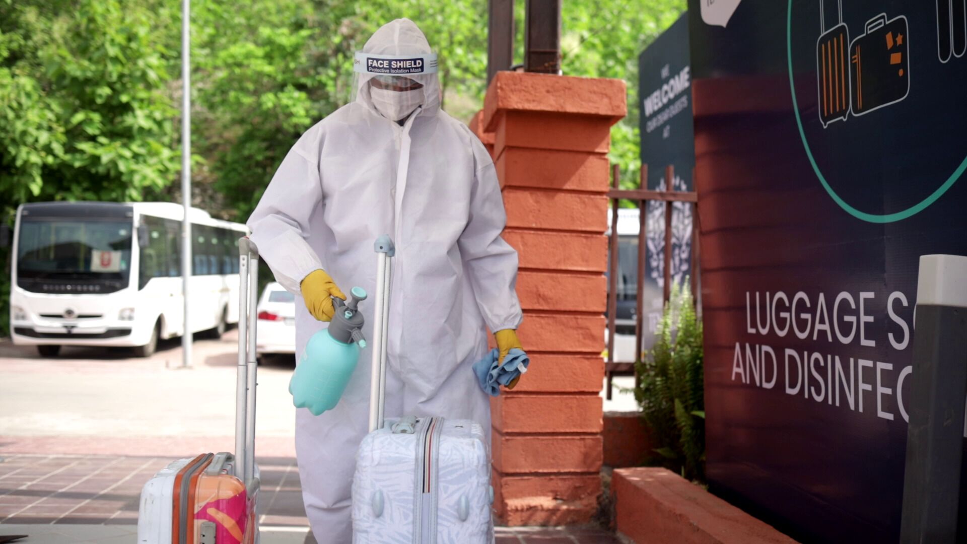 A person in protective gear with luggage, standing near a sign for luggage and disinfection services.