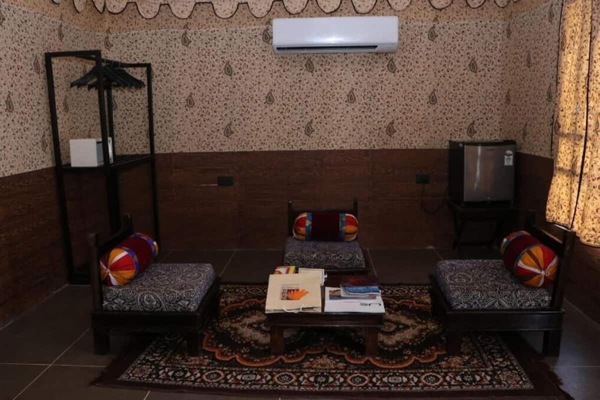 A room with patterned wallpaper, a sofa set, a small table with books, an air conditioner, and a television.