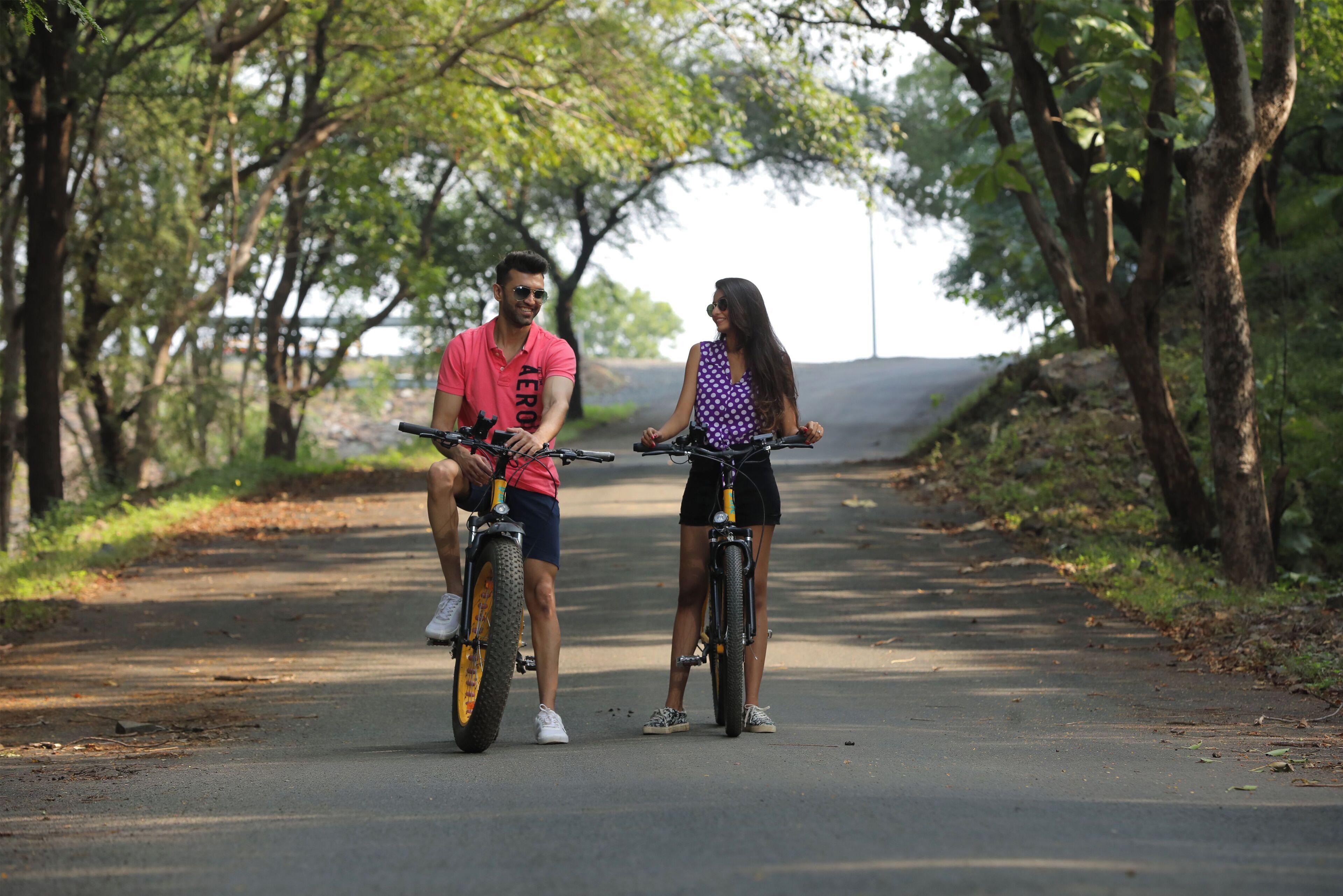 Dos personas en bicicleta sobre un camino pavimentado, rodeado de árboles.