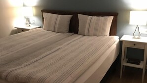A neatly made bed with striped bedding, two bedside tables with lamps, and a wooden floor. - Skipholt (Vogar)