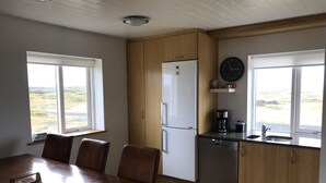 A compact kitchen with a refrigerator, coffee maker, and sink. There is a dining table with chairs and a window providing a view of the outdoors. - Skipholt (Vogar)