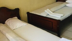 Quarto com duas camas individuais, cada uma com cabeceira de madeira e roupa de cama branca.
