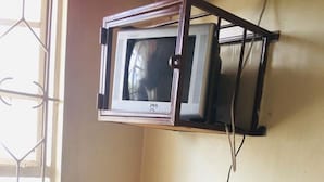 Um quarto com uma escrivaninha de madeira, uma cadeira e uma televisão fixada na parede.