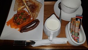 Un vassoio colazione con pane tostato, fagioli, salsicce, una tazza di latte e una ciotola di cereali.