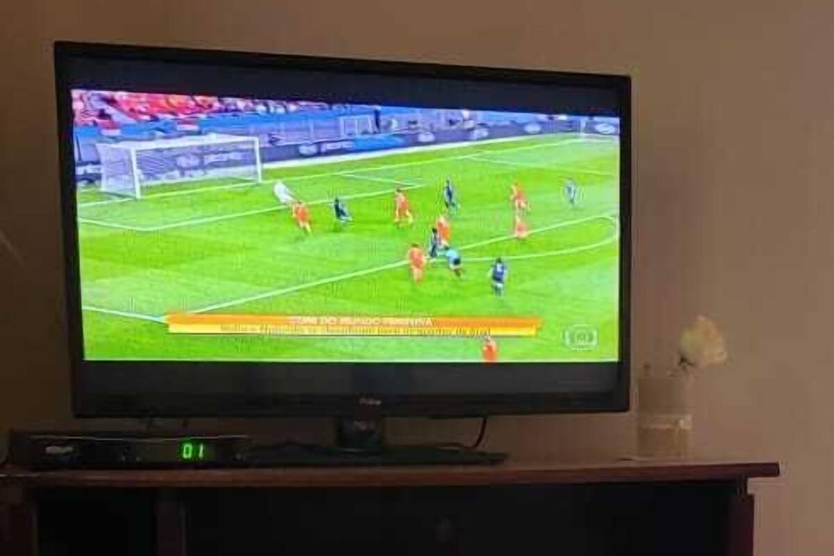 Een televisie op een houten standaard waarop een voetbalwedstrijd te zien is.