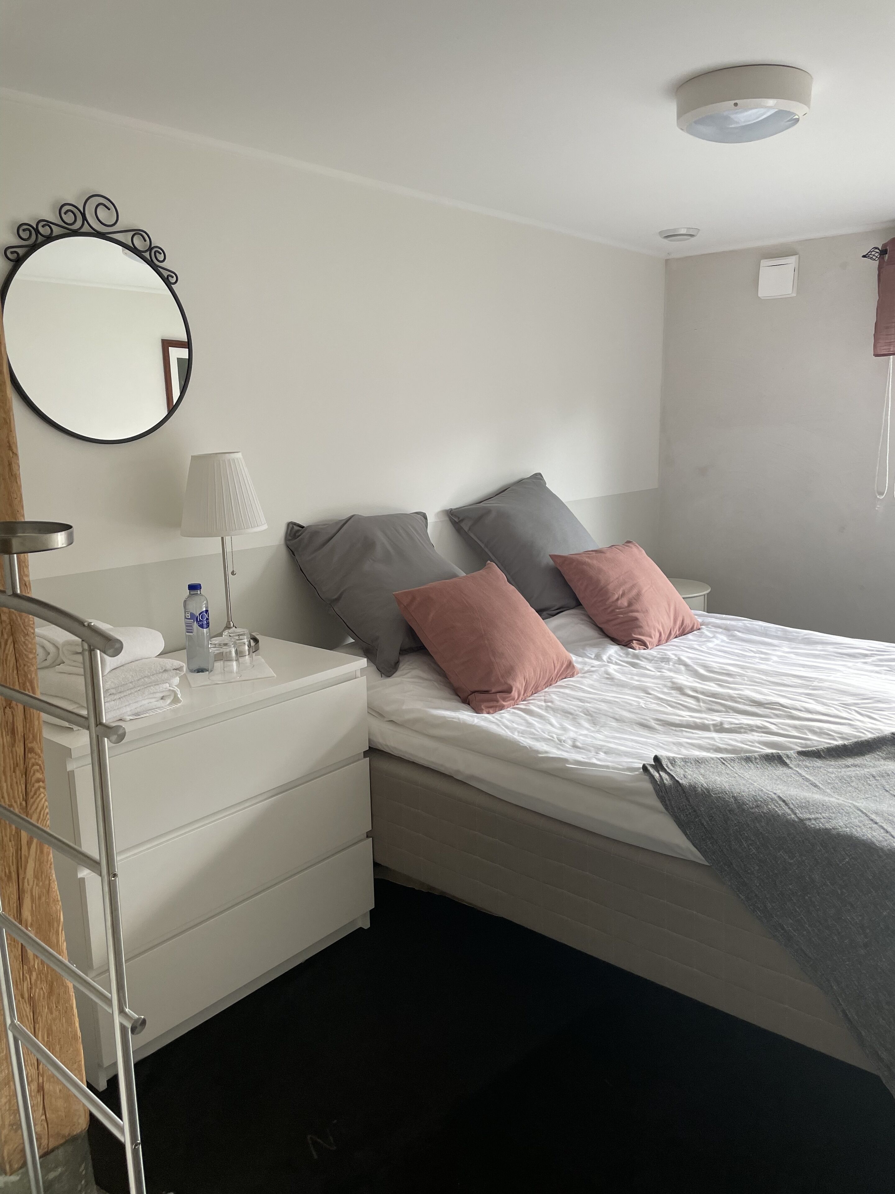 A neatly arranged bedroom with a bed, bedside tables, a mirror, and a wall-mounted air conditioning unit.