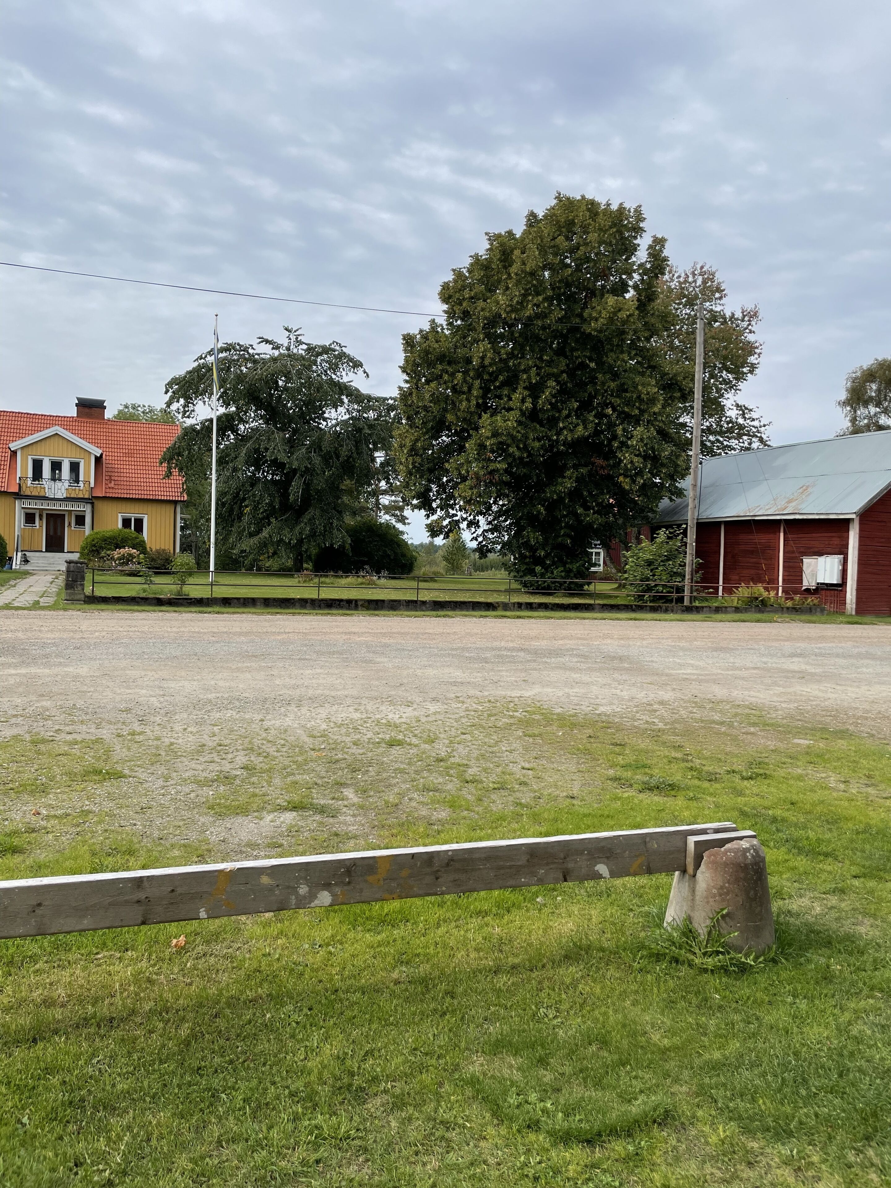 A rural setting with a large open field, a yellow house with a red roof, and a red barn.