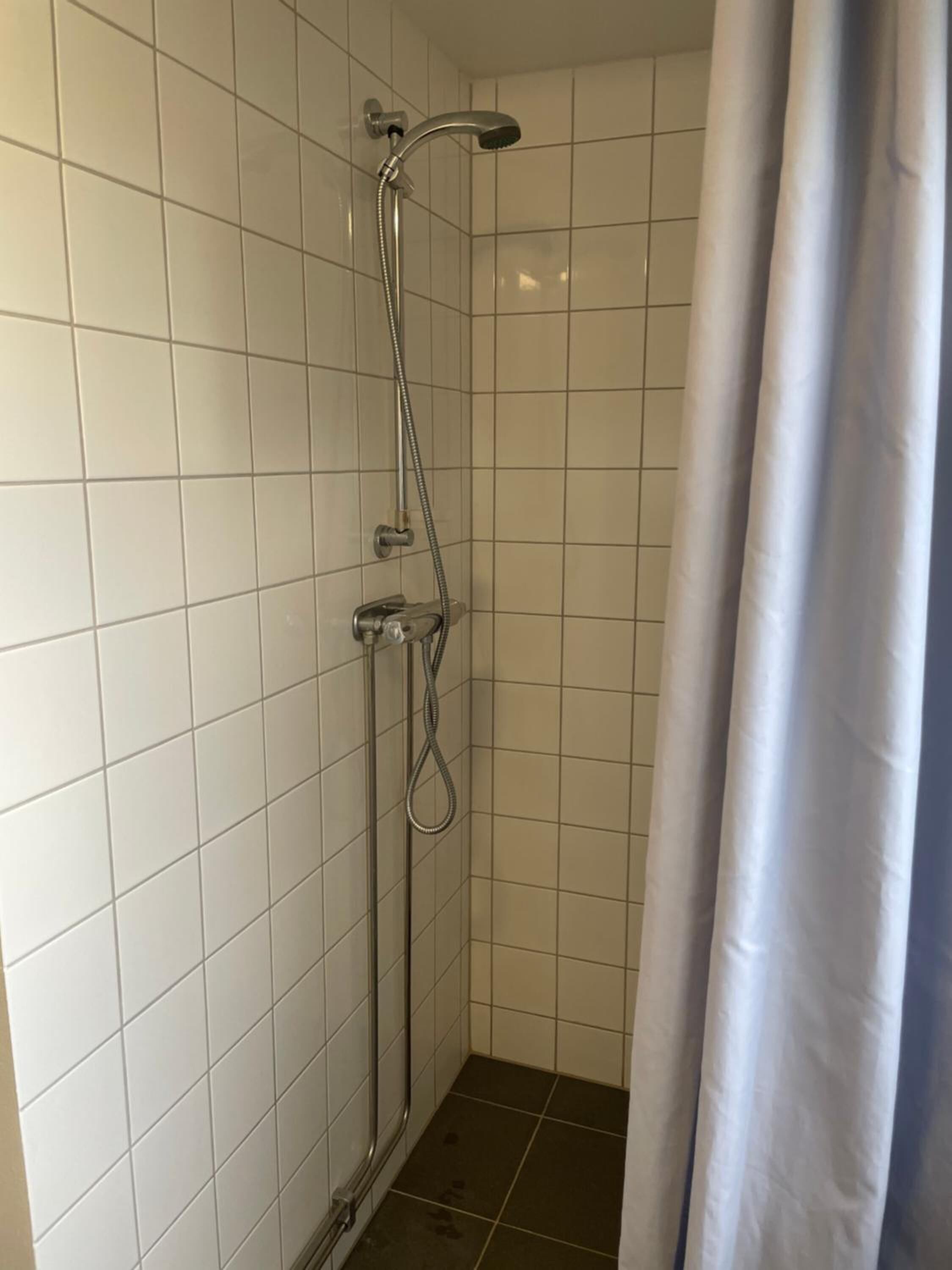 A small, tiled shower room with a showerhead and faucet.