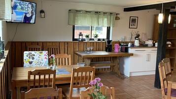 A cozy dining area with wooden furniture, a television mounted on the wall, and a window with curtains.