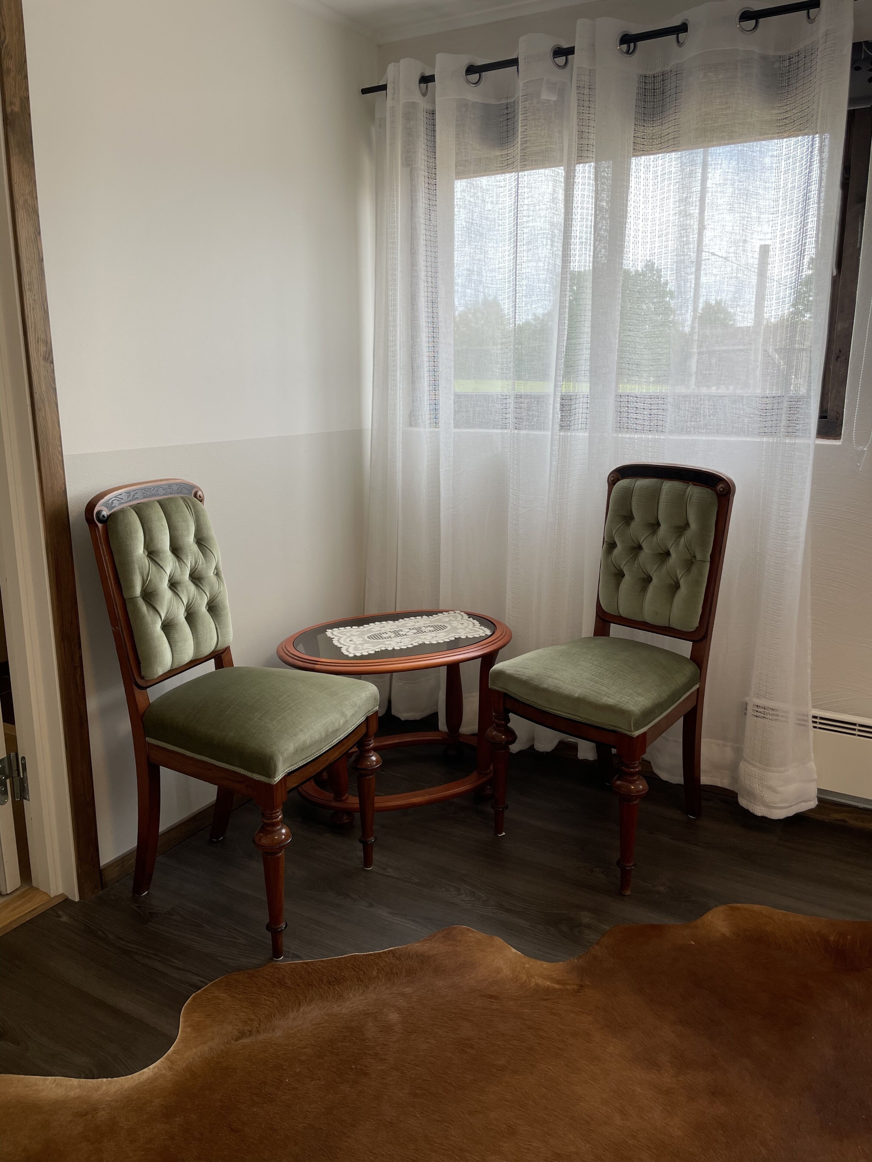 Quarto com duas poltronas estofadas, com estrutura de madeira, e uma mesinha redonda com um toalhinha branca.