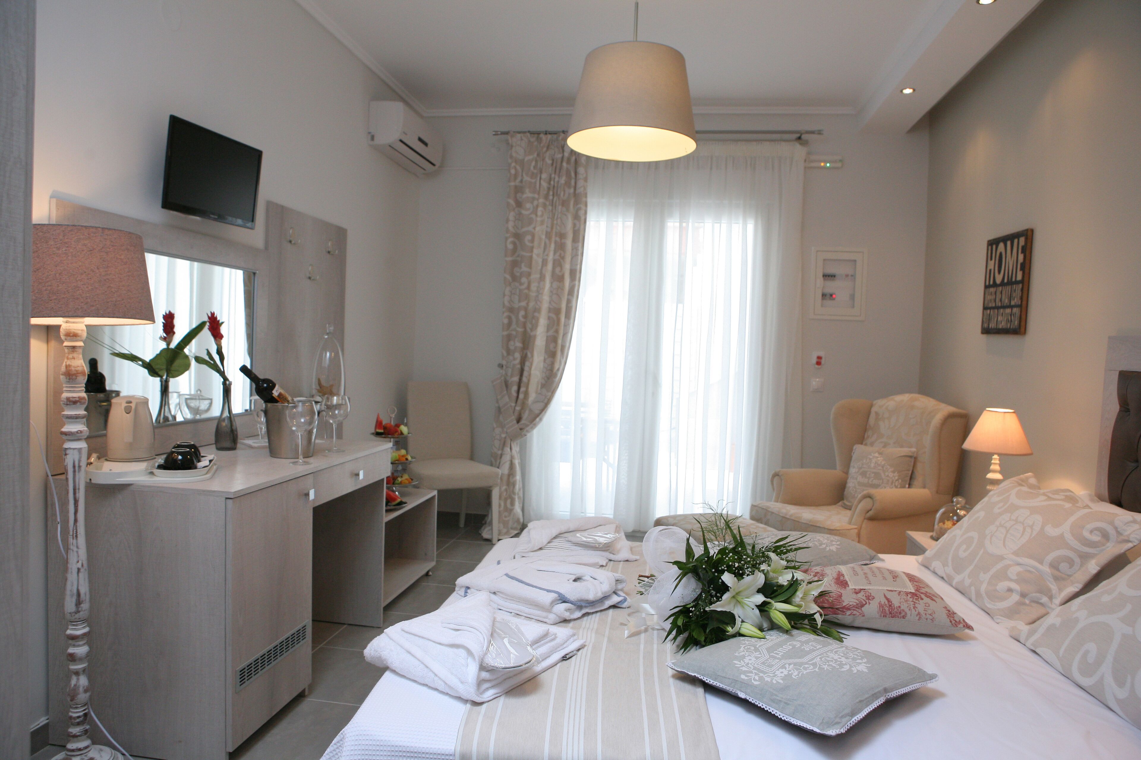 Habitación de hotel con cama, dos sillas, escritorio con lámpara, televisión y ventana con cortinas.