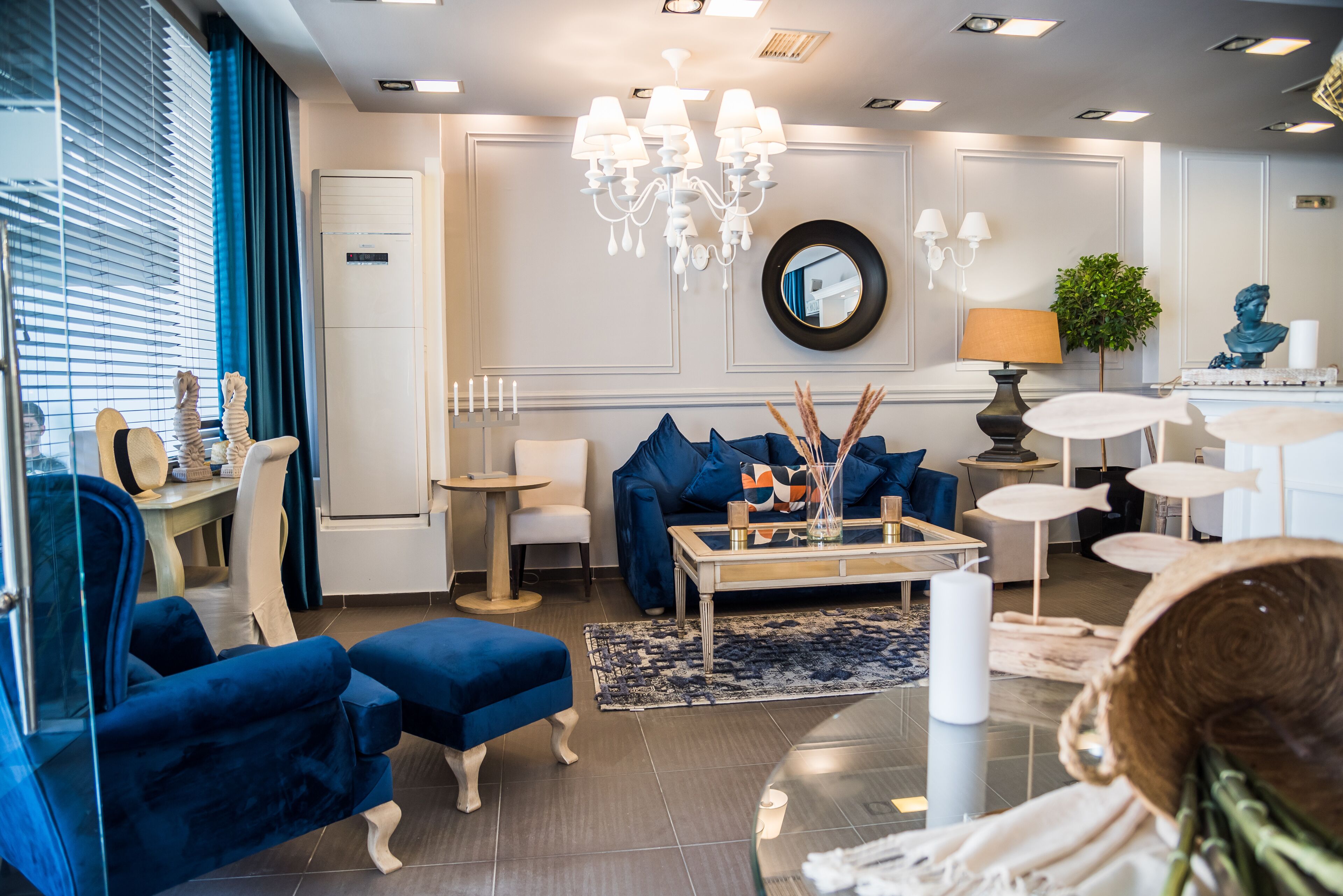 A modern living room with a blue sofa, a glass coffee table, and a chandelier.