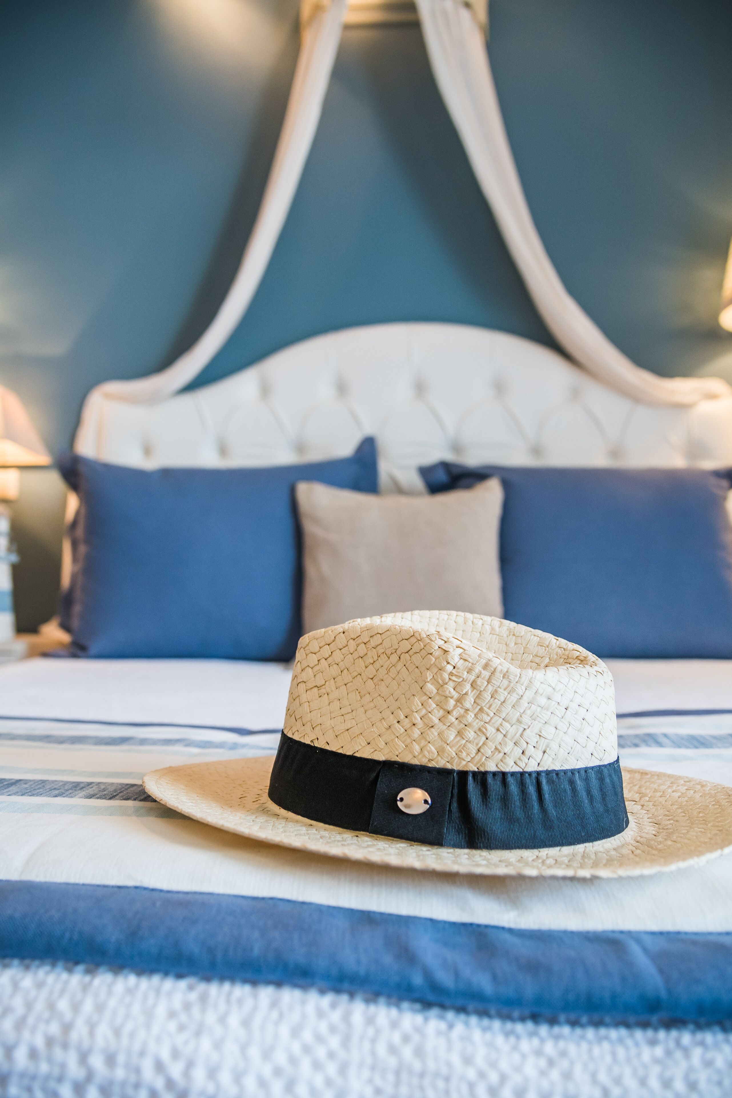 Un lit recouvert d’une couvre-lit à rayures bleues et blanches, un lit à baldaquin blanc et un chapeau de paille posé sur le lit.
