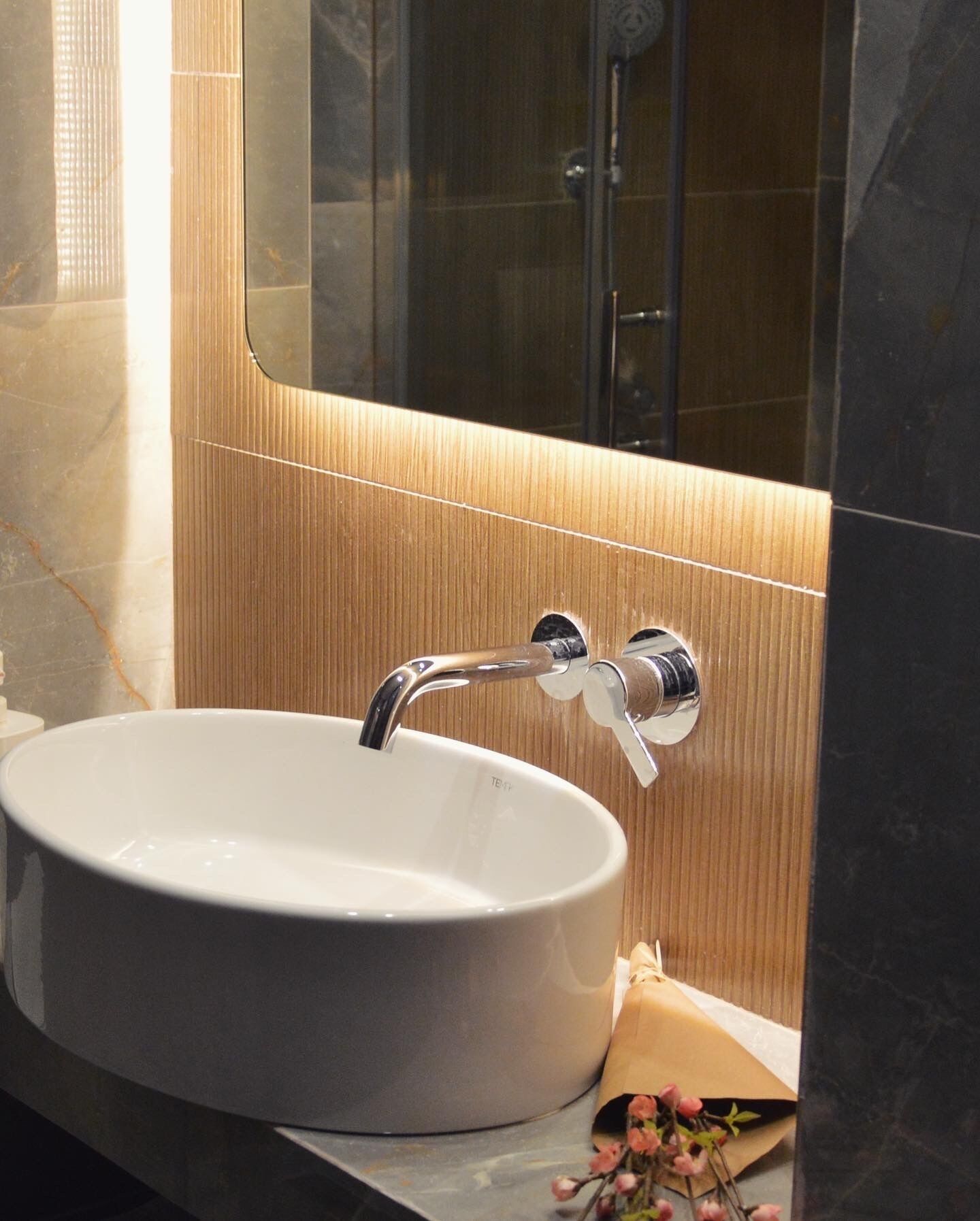 Un baño con un lavamanos redondo blanco, grifo cromado y un espejo encima.
